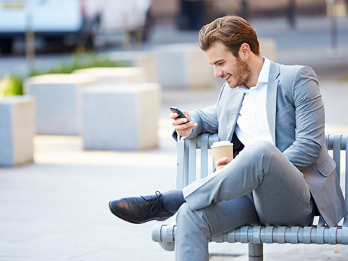 Geschaeftsmann sitz auf einer Bank und liest auf seinem Smartphone