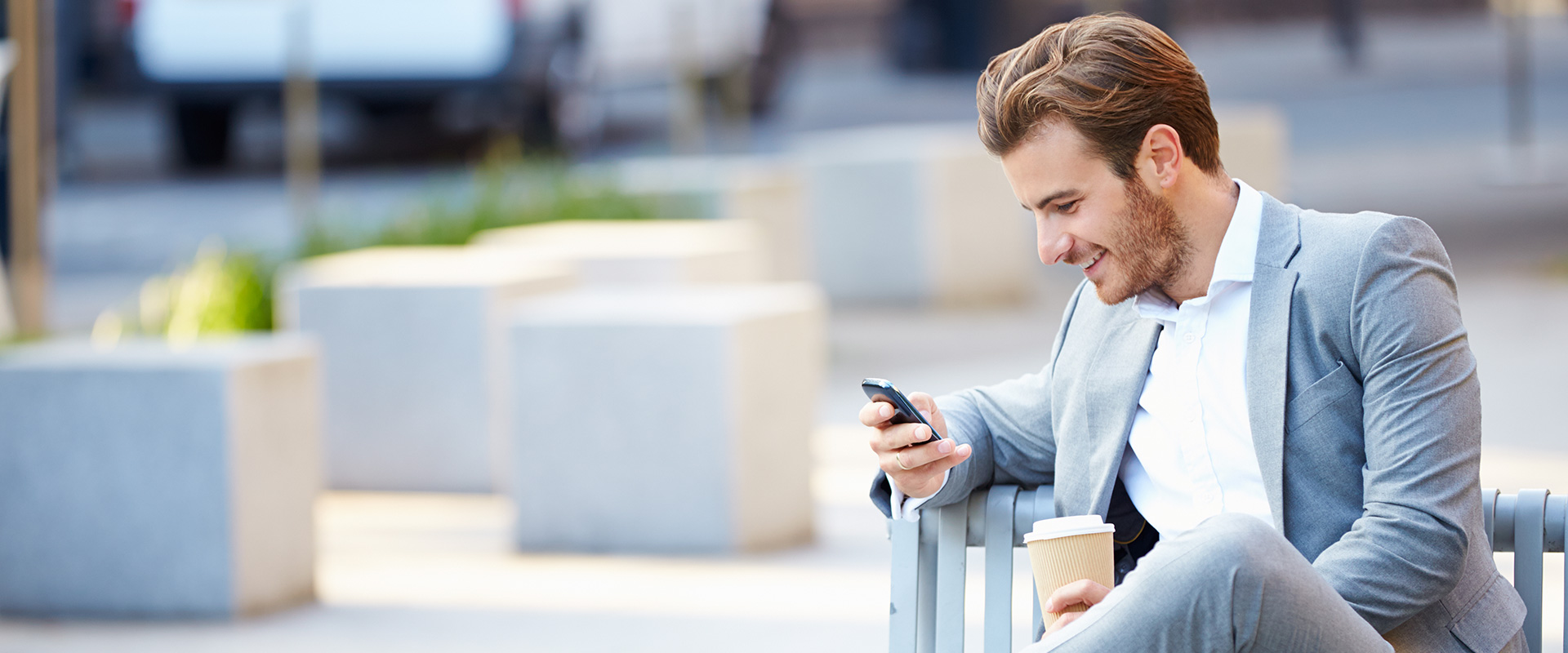 Geschaeftsmann sitz auf einer Bank und liest auf seinem Smartphone