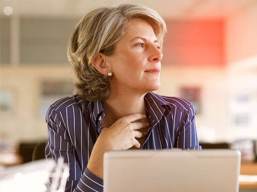 Eine Geschaeftsfrau sitzt vor dem Laptop und schaut nachdenklich zur Seite